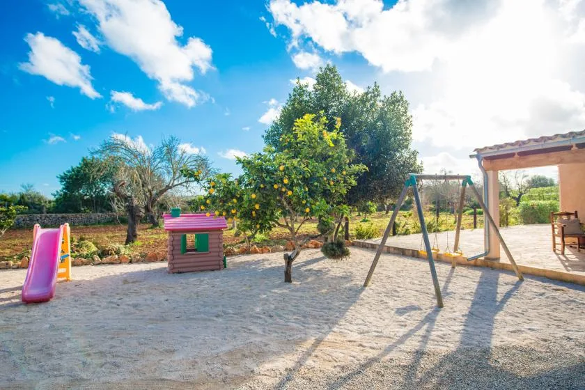 An outdoor play area with a small playhouse, slide, and swing set.