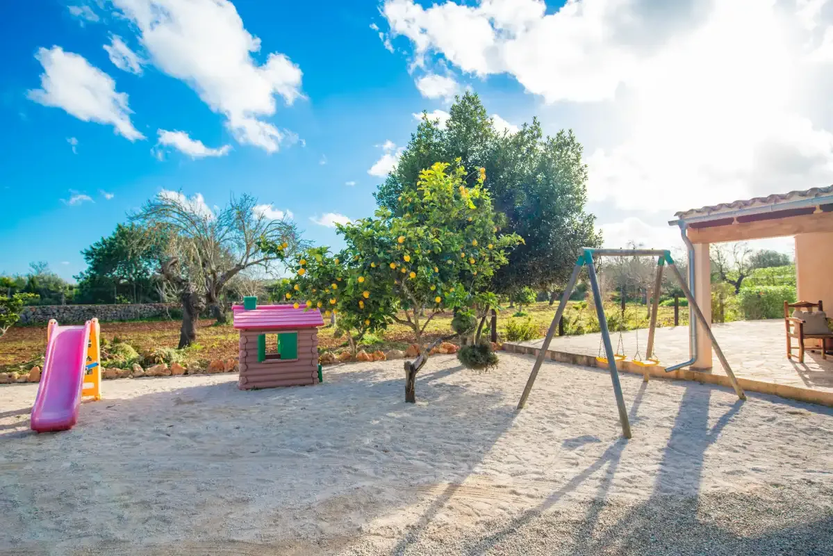 A sandy outdoor play area with a swing set, slide, and small playhouse.