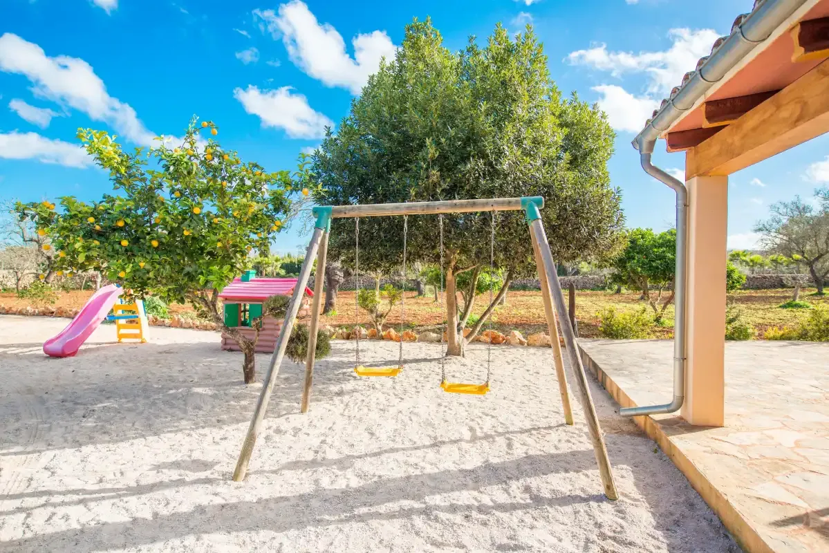 An outdoor play area has a swing set, a small slide, and a tree.