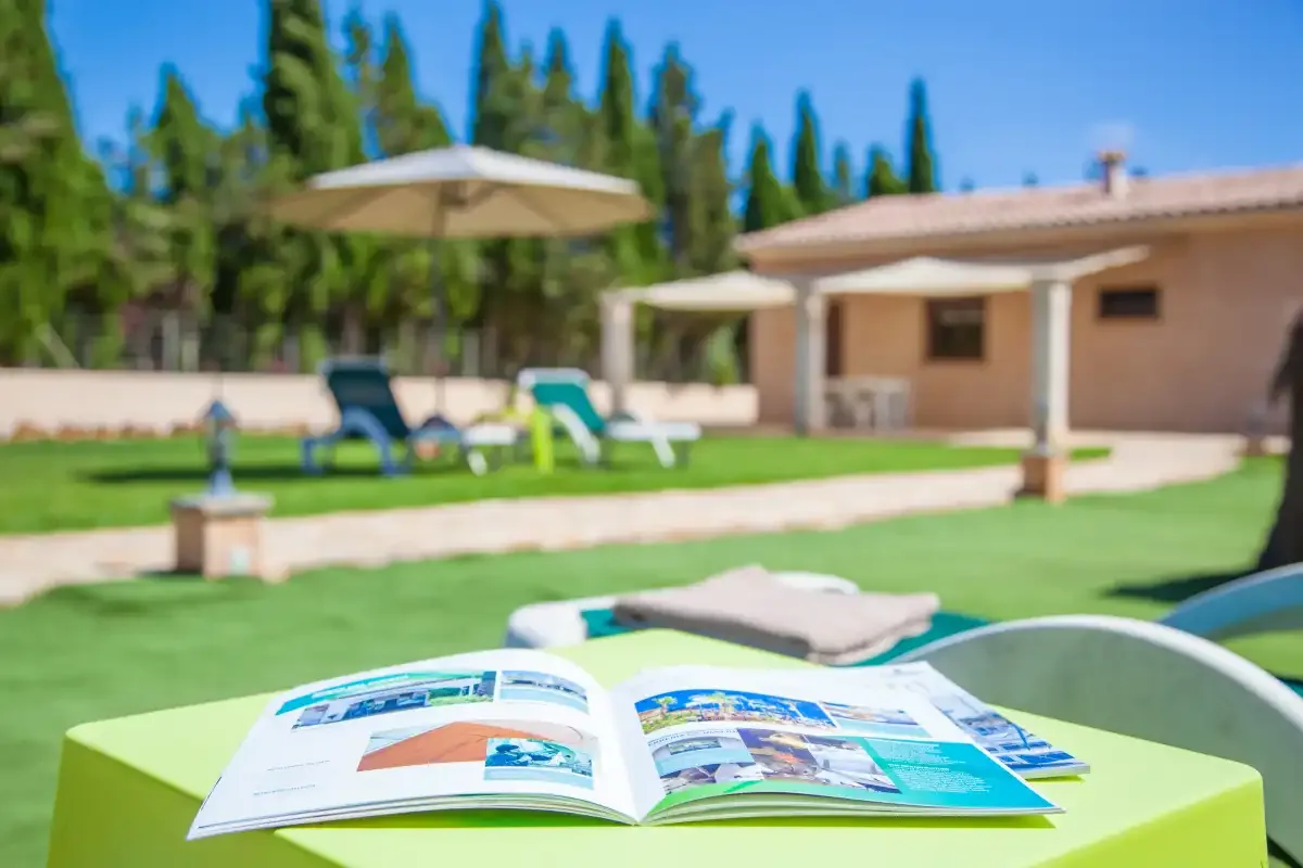 A garden patio with an open brochure on a bright table, lawn, and outdoor seating.