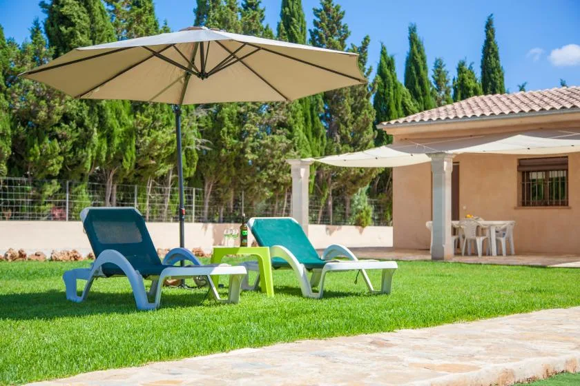 Un patio con césped, asientos reclinables, sombrillas y una zona de comedor cubierta.