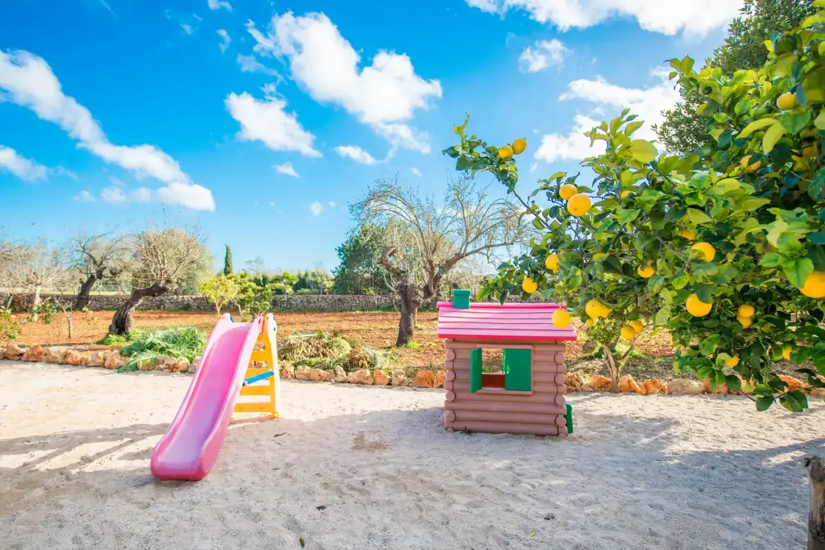 A sandy outdoor play area with a slide and a small playhouse.