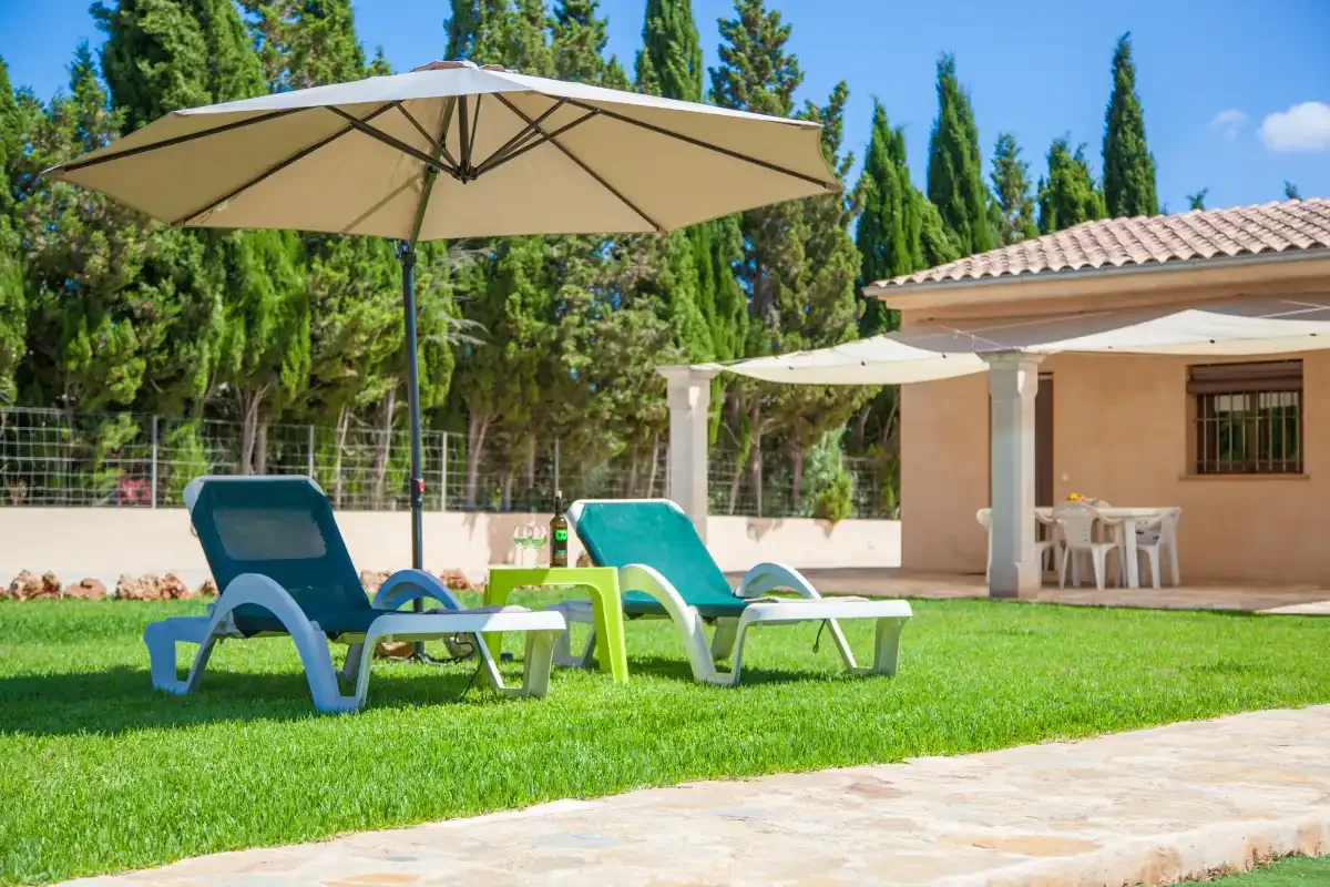 A grassy outdoor patio with lounge seating, umbrellas, and a small building.