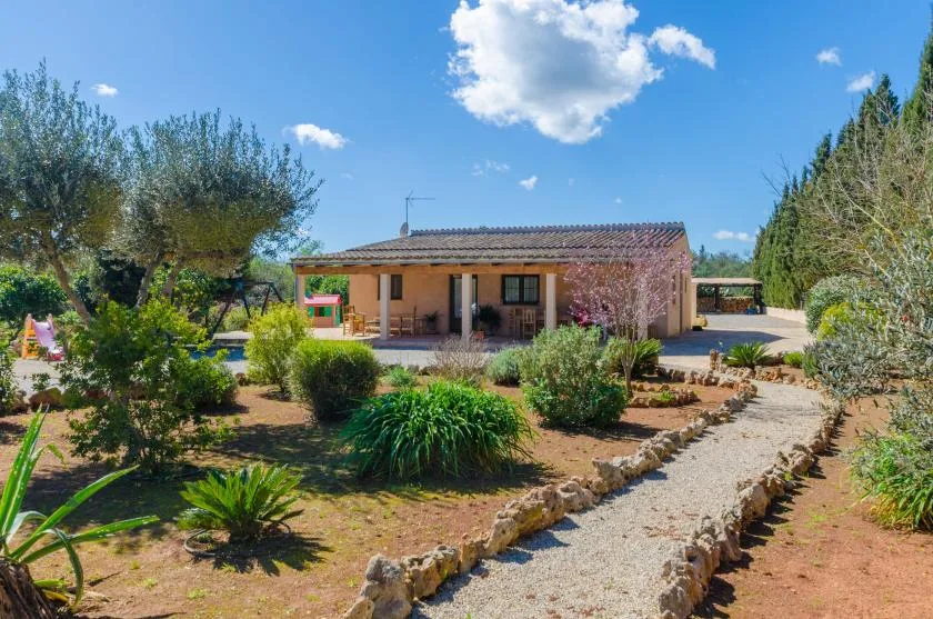 Una casa de una planta se encuentra detrás de un sendero de grava bordeado de plantas.