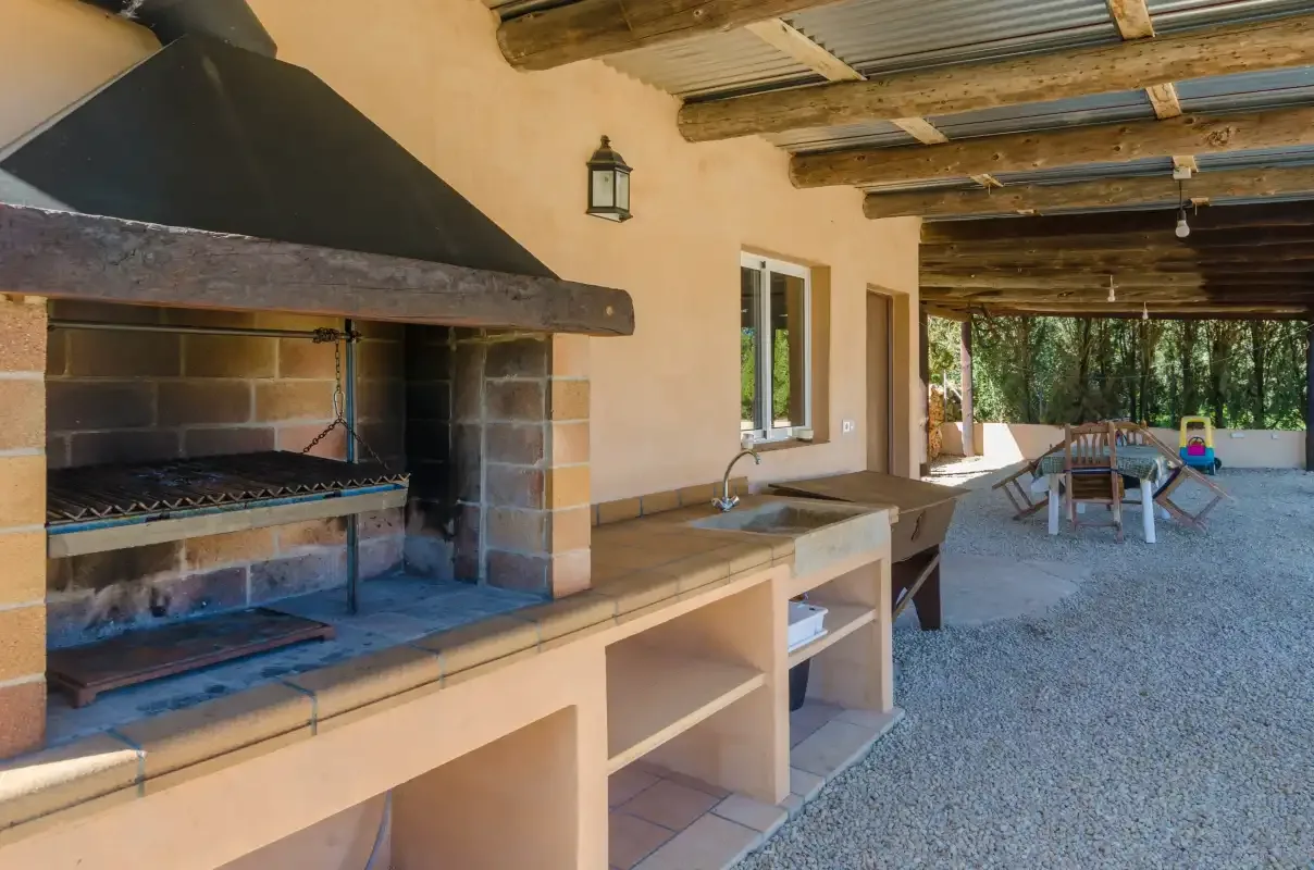 A covered outdoor dining area with a built-in barbecue and table.