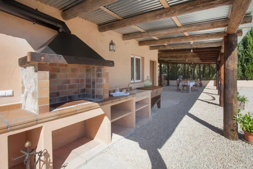 Zona cubierta de cocina y comedor al aire libre, con parrilla integrada y mesa.