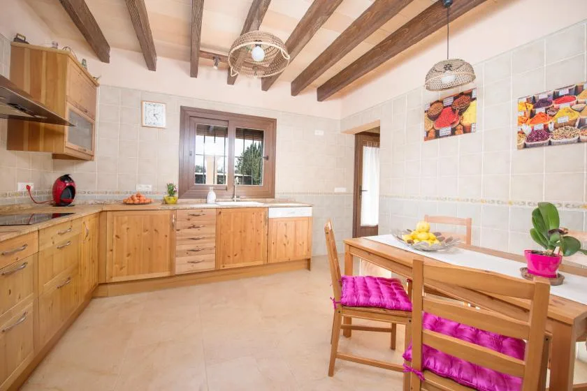A bright kitchen with wooden cabinets, a dining table, and exposed ceiling beams.