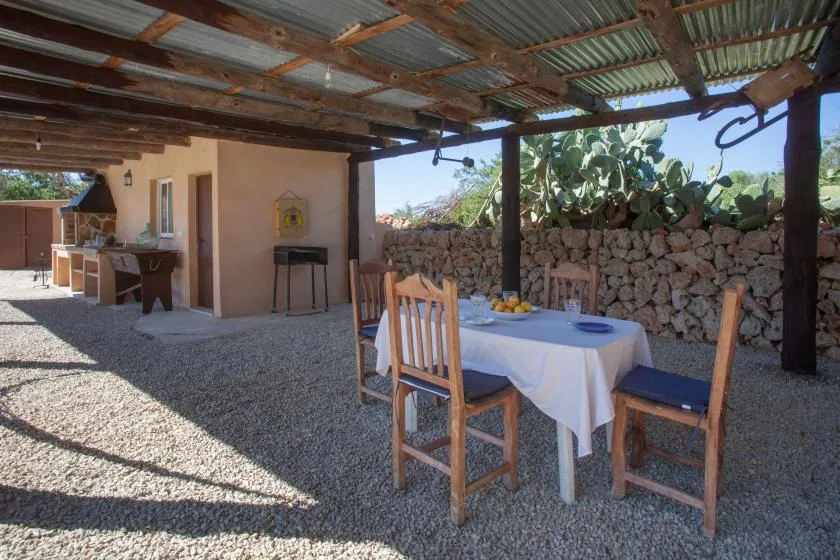 A covered outdoor dining area with a table, chairs, and a stone wall.