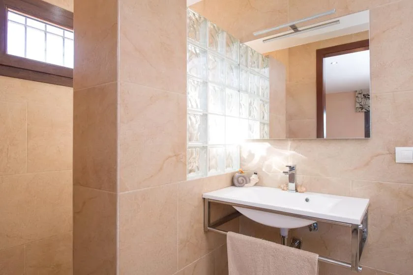 A bathroom vanity sits beside a glass-block window and wall mirror.