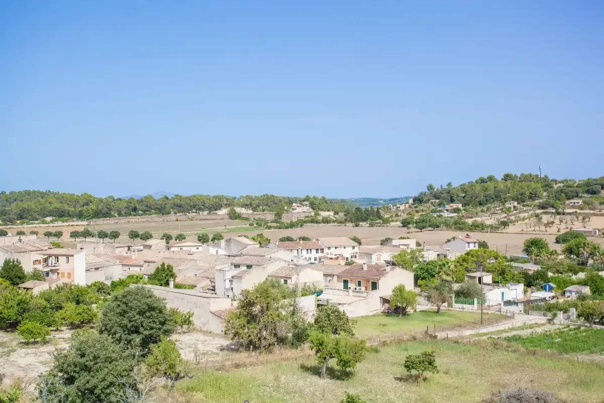 A rural village spreads across a green landscape beneath a clear blue sky.