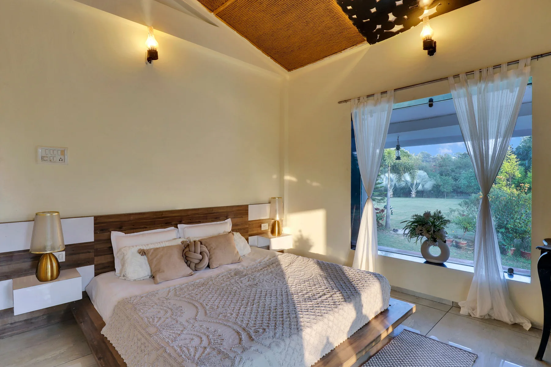 A bedroom with a large bed beside a window overlooking greenery.