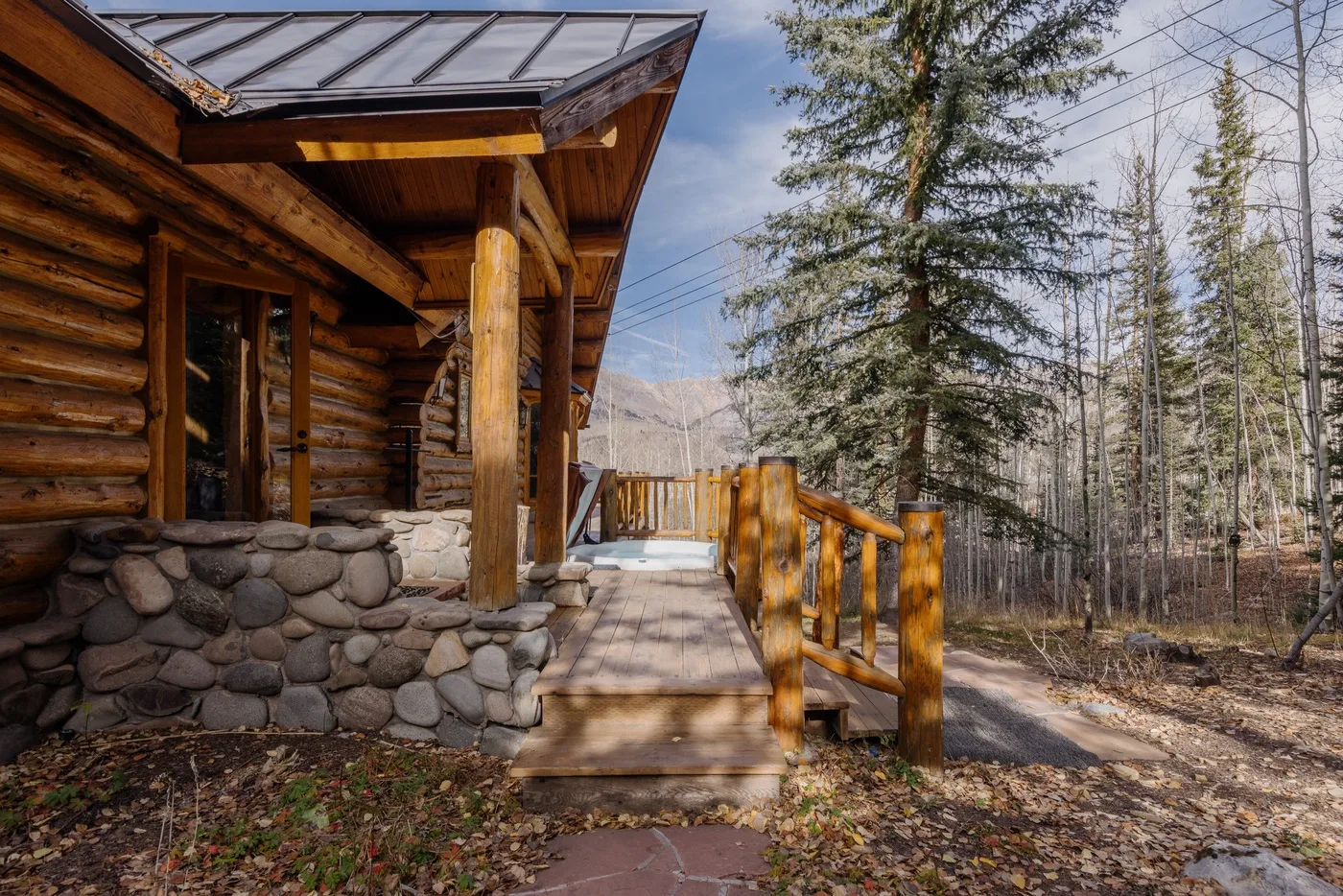 A wooden cabin porch with log walls and a walkway through a wooded setting.