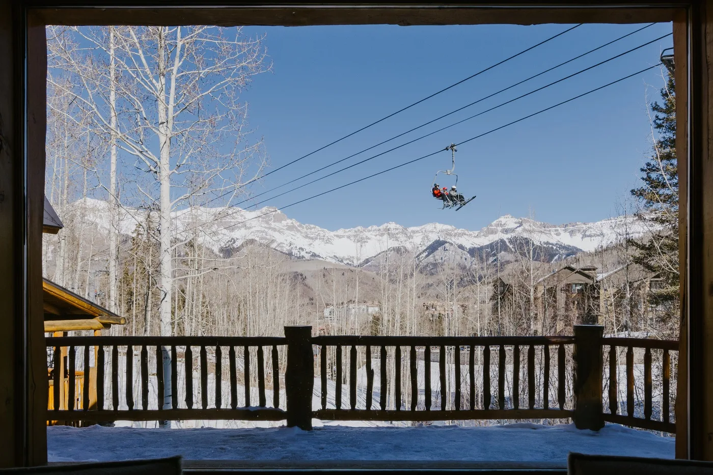 A mountain view from a wooden deck, with ski lifts crossing the snowy peaks.