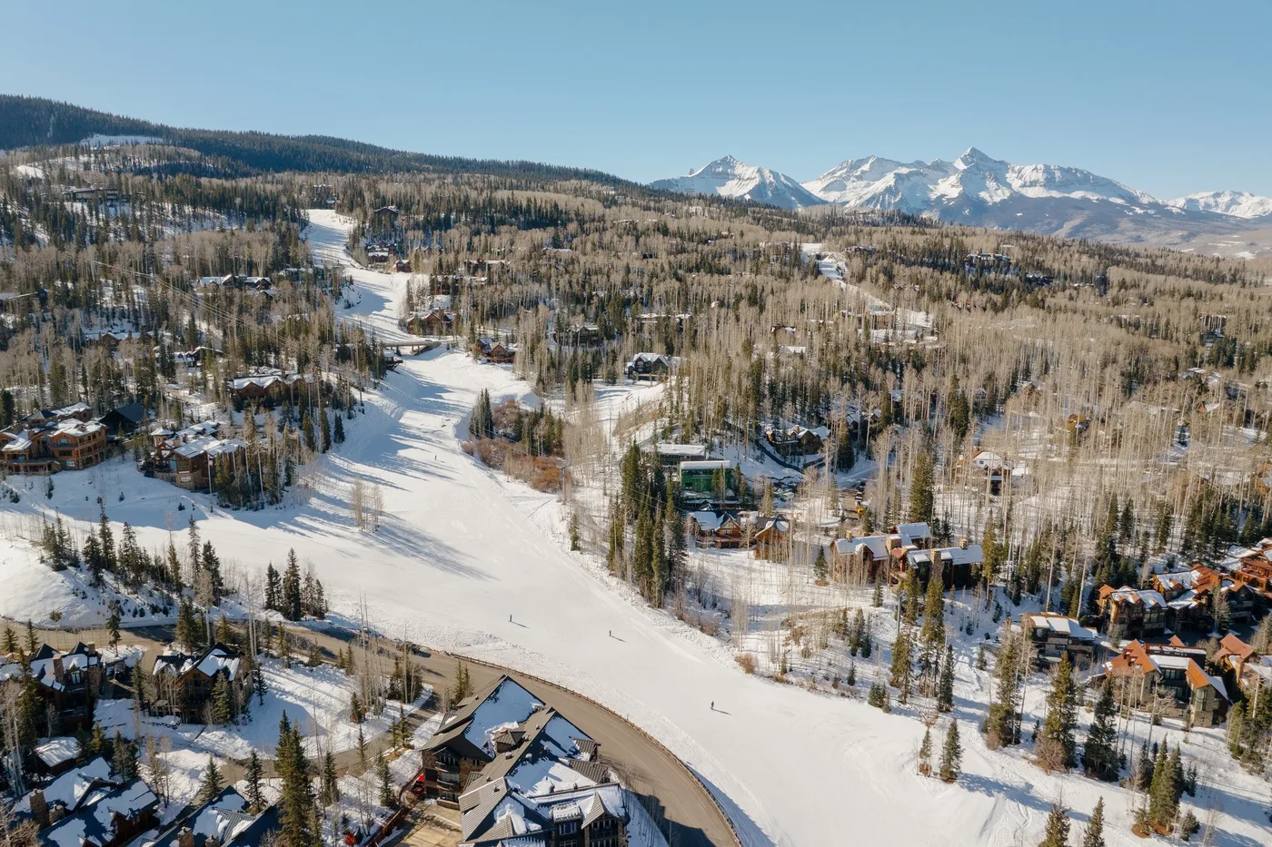 Aerial view of a snowy ski slope winding through a wooded mountain resort.