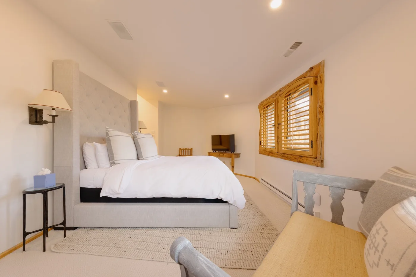 A bright bedroom with a large bed, a television, and a wooden window blind.
