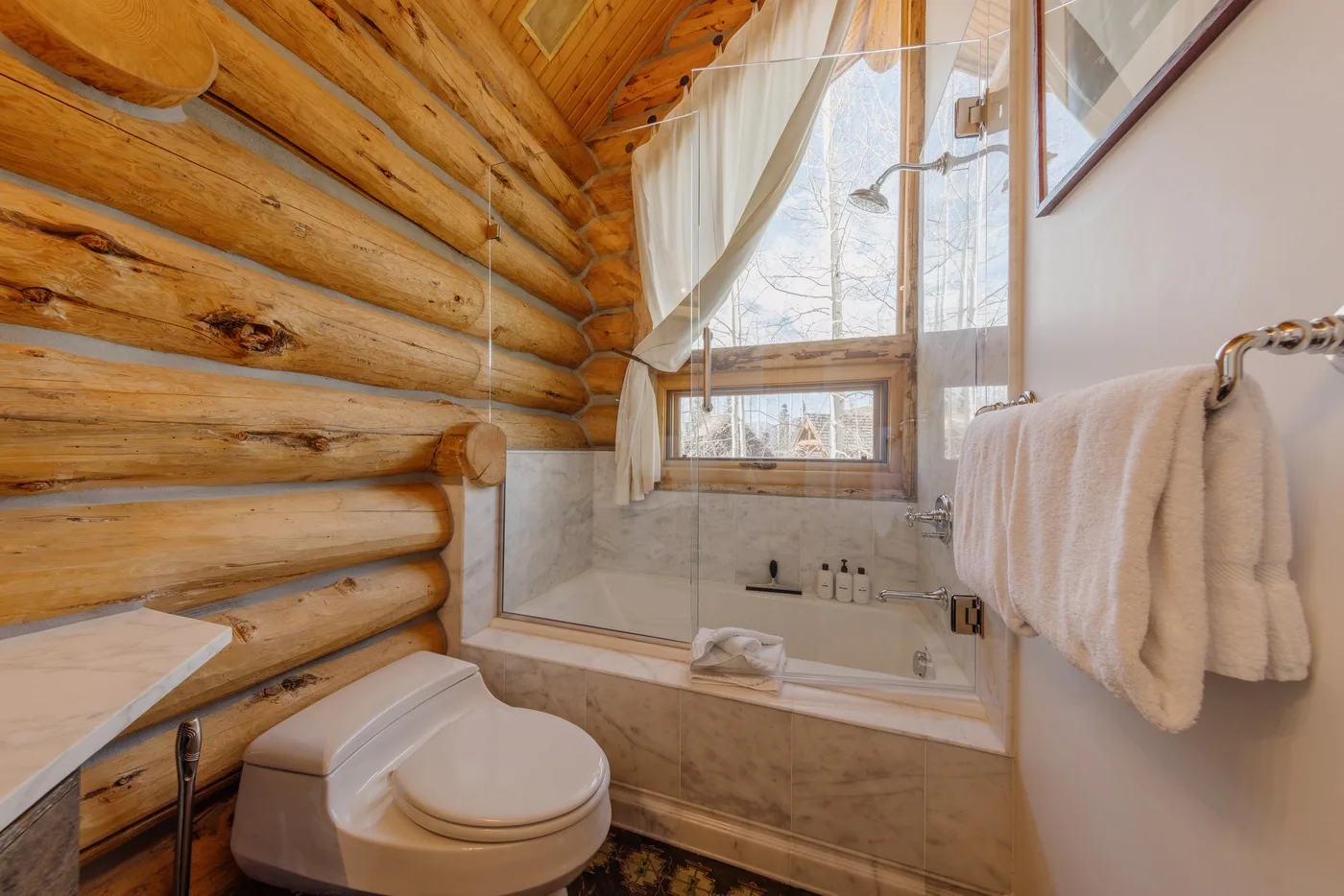 A bathroom with a bathtub, shower, and toilet beside a log wall.