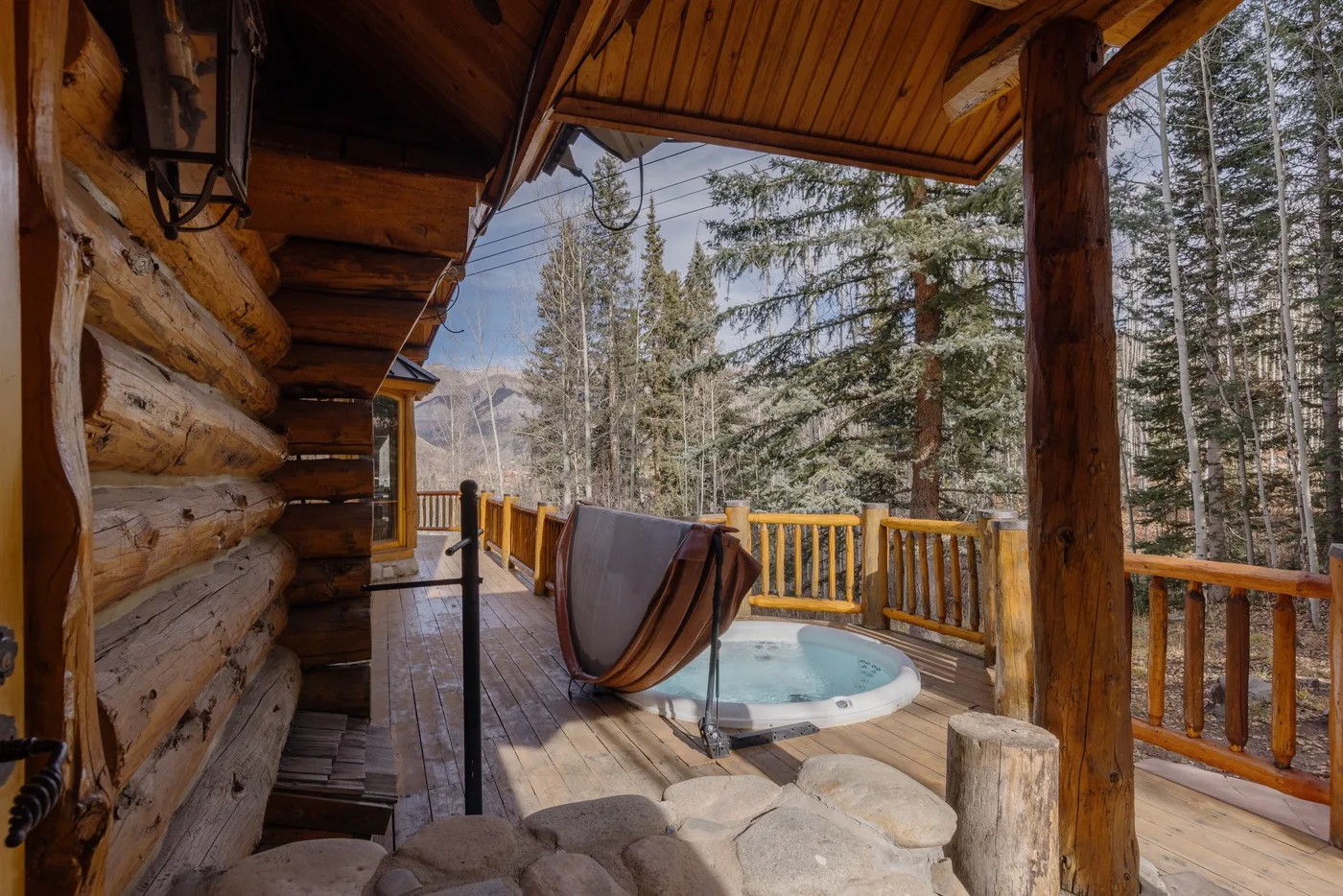 A wooden porch overlooks a forest, with a small outdoor hot tub nearby.