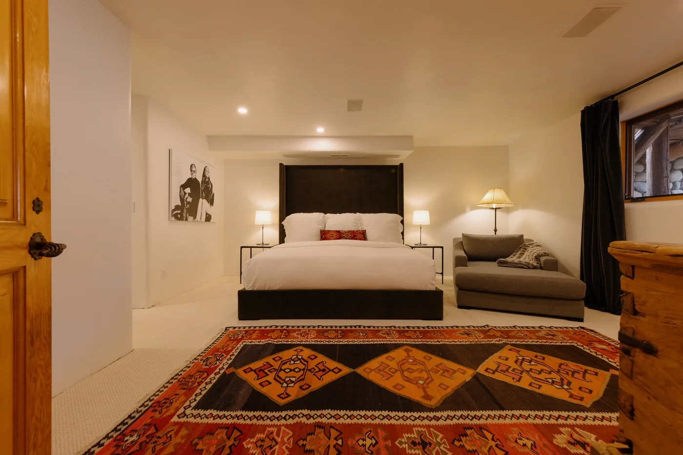 A bedroom with a neatly made bed, a rug, and a chair beside the window.