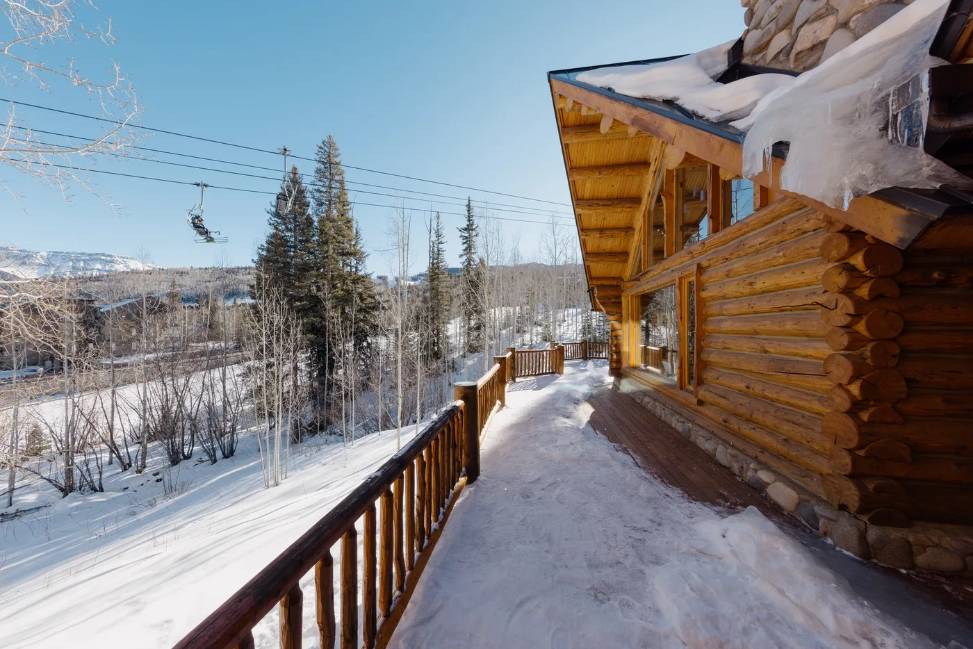 A snow-covered deck runs alongside a log cabin overlooking a winter landscape.