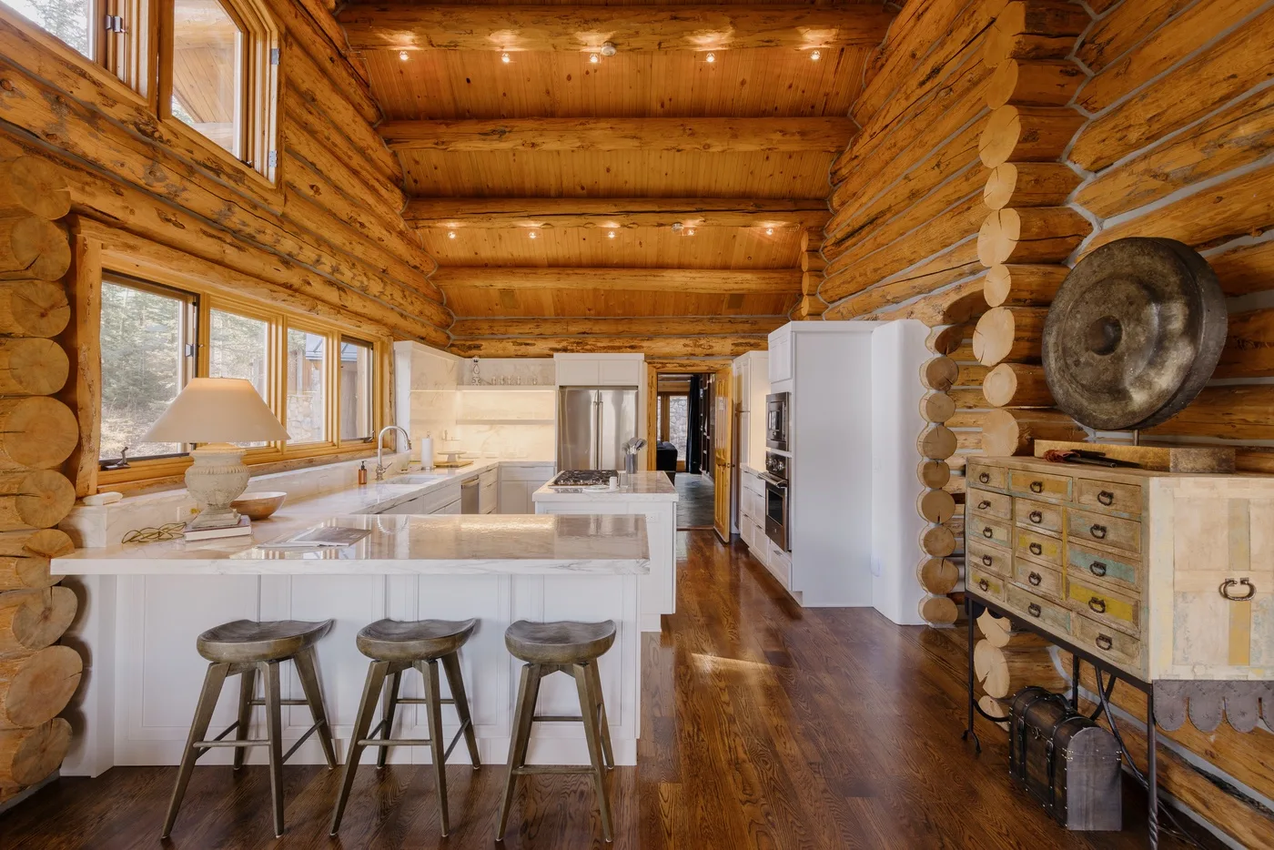 A log cabin kitchen with a white island, stools, and stainless-steel appliances.
