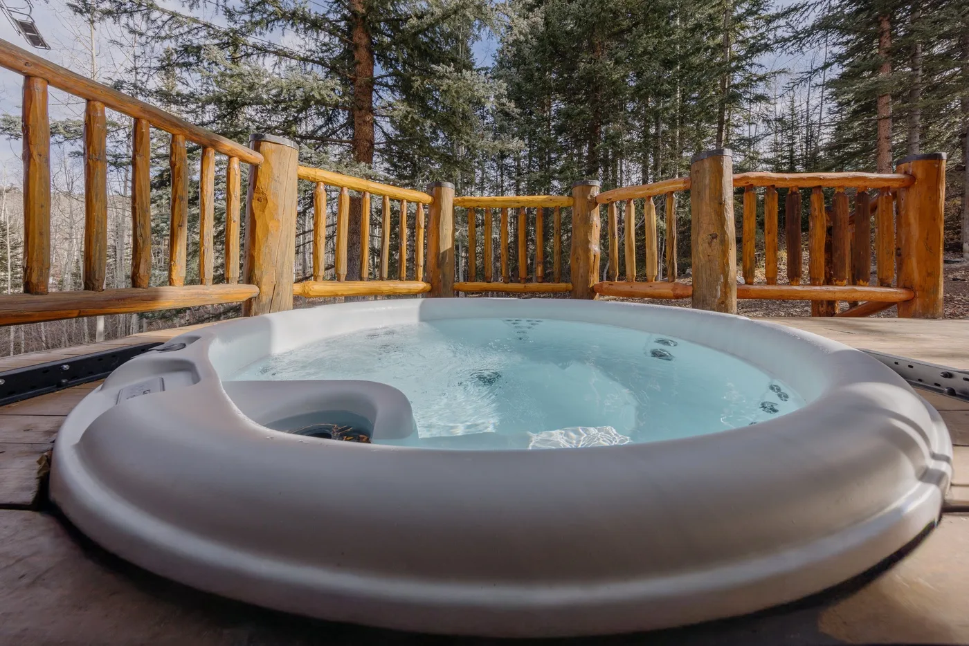 An outdoor hot tub sits on a wooden deck surrounded by trees.