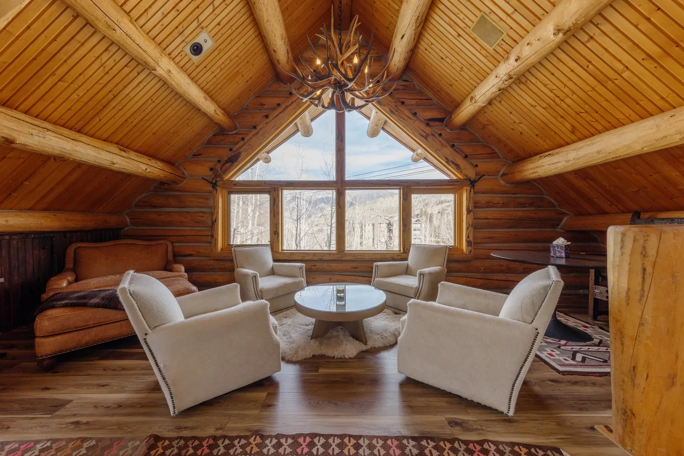 A wood-paneled living room with seating arranged around a low table beneath large windows.