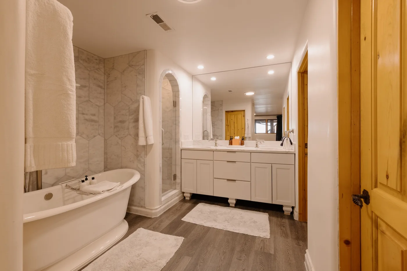 A bright bathroom with a bathtub, vanity, and pale floor mats.