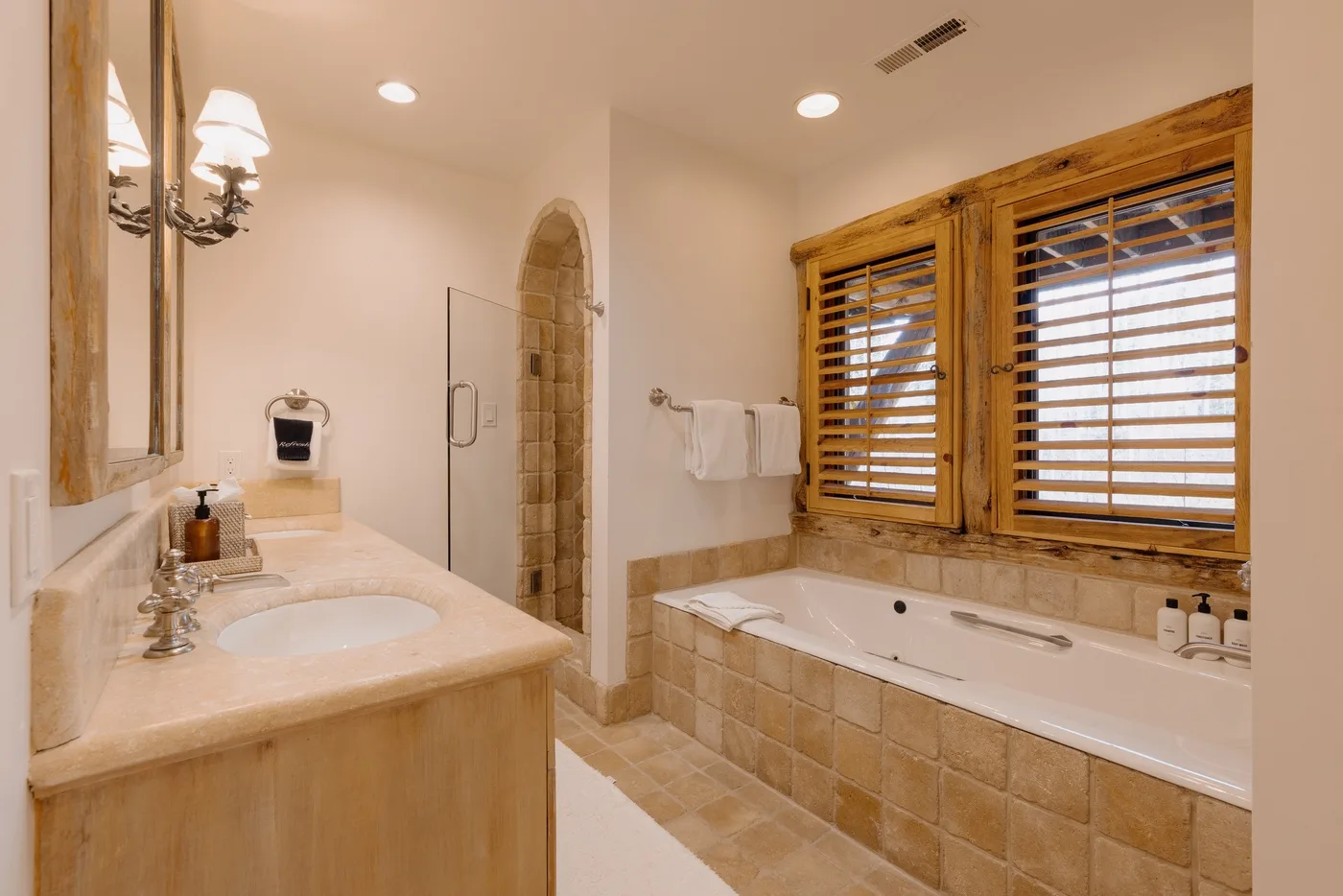 A bathroom with a bathtub beneath wooden windows and a sink.