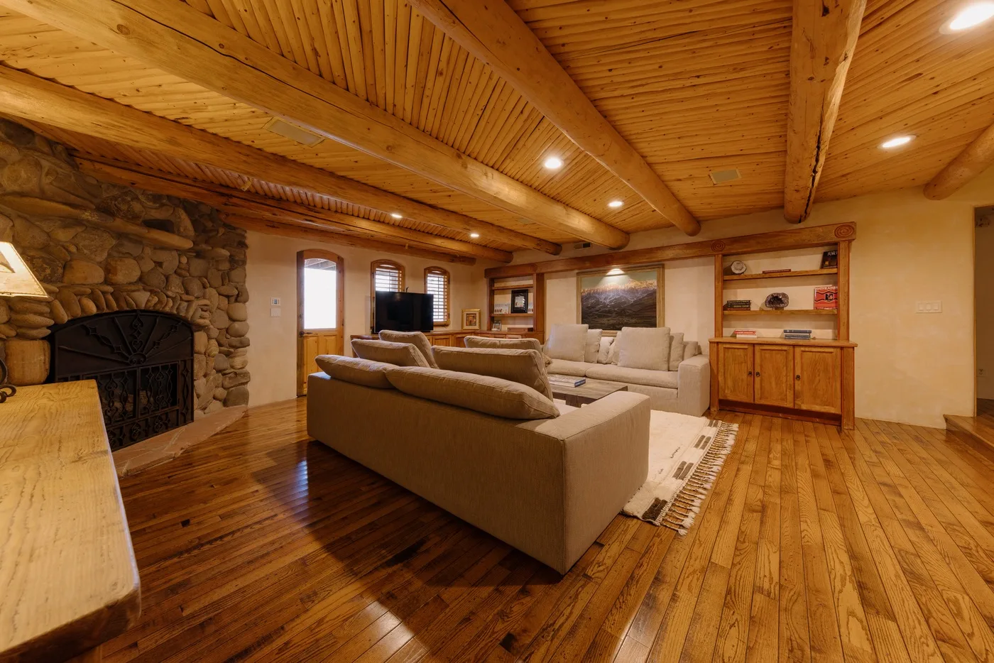 A living room with seating arranged around a fireplace beneath a wood-paneled ceiling.