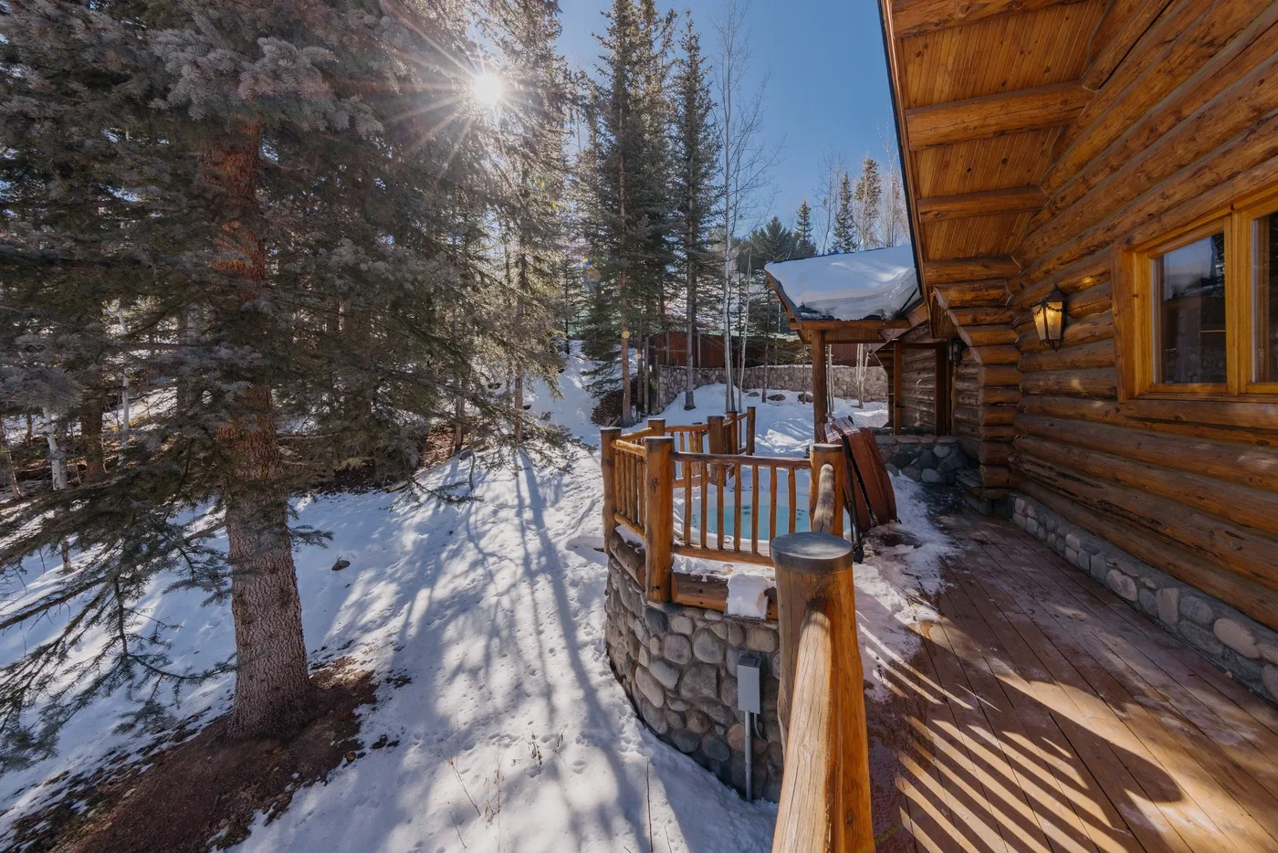 A wooden deck beside a log cabin overlooks a snowy, tree-lined outdoor scene.