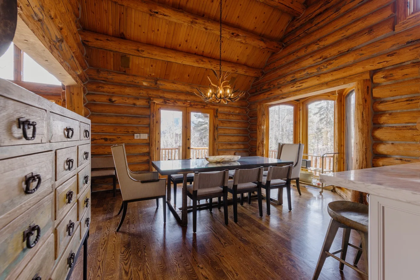 A dining area with a long table and large windows in a wood-paneled room.