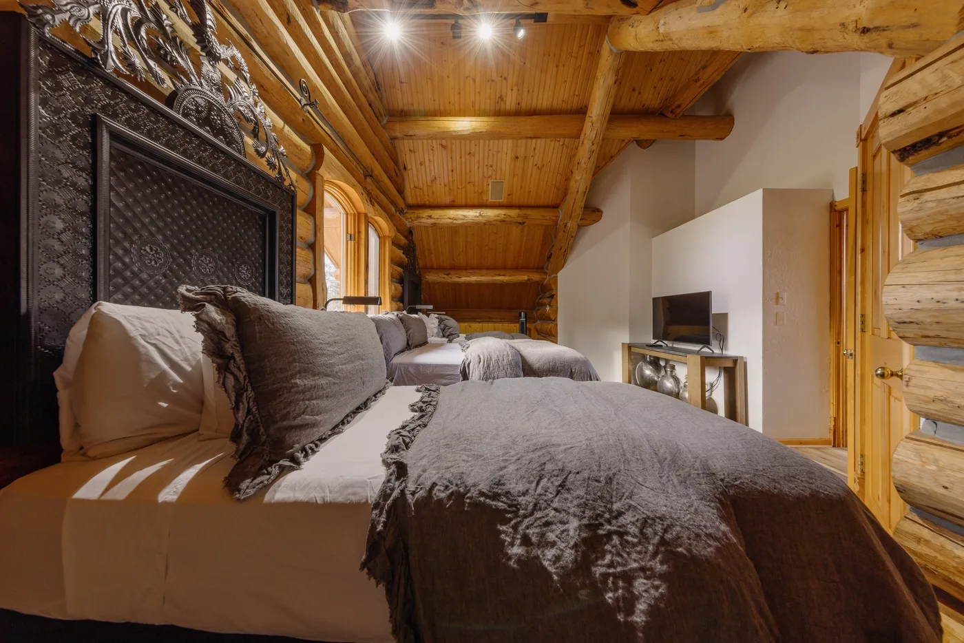 A bedroom with beds beneath a sloped wooden ceiling and a television.
