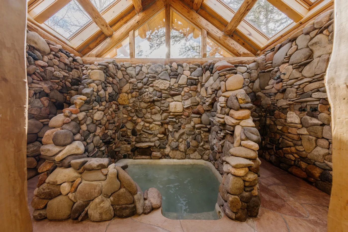 A stone-walled indoor pool sits beneath a timber-framed glass roof.