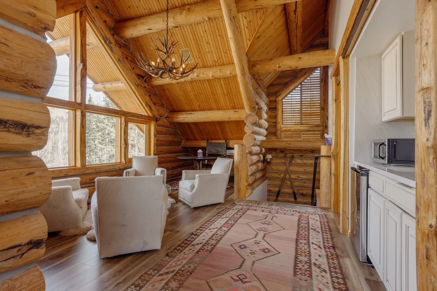 A timber living room with seating, large windows, and a patterned rug.