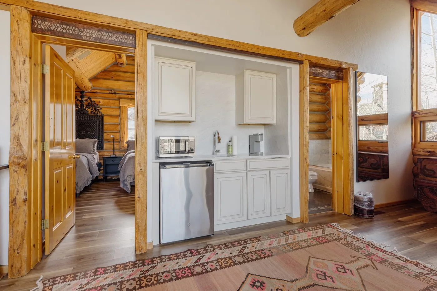 A wood-trimmed room with a compact kitchenette and an open doorway to a bedroom.