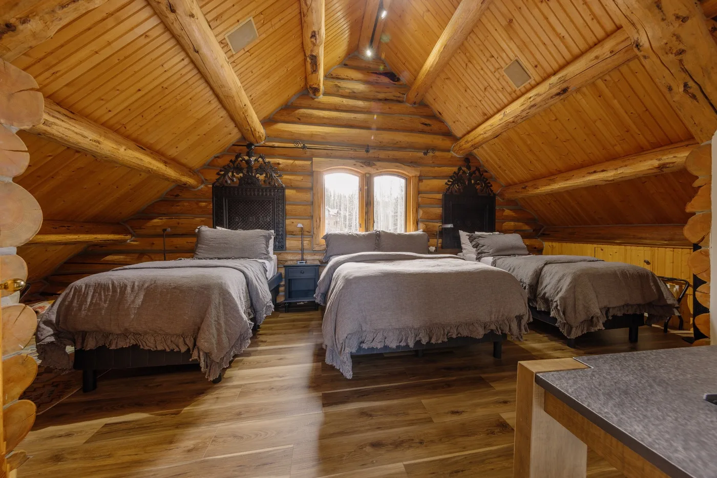 A wood-paneled attic bedroom with three beds beneath a pitched timber ceiling.