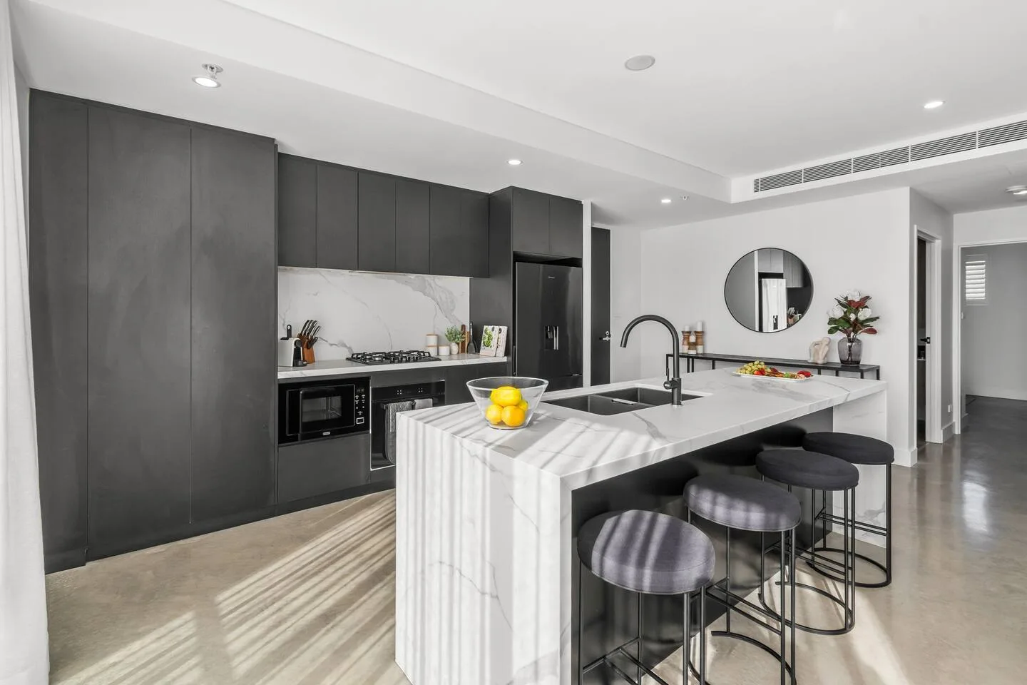 A modern kitchen features dark cabinetry, a large island, and stools at the counter.