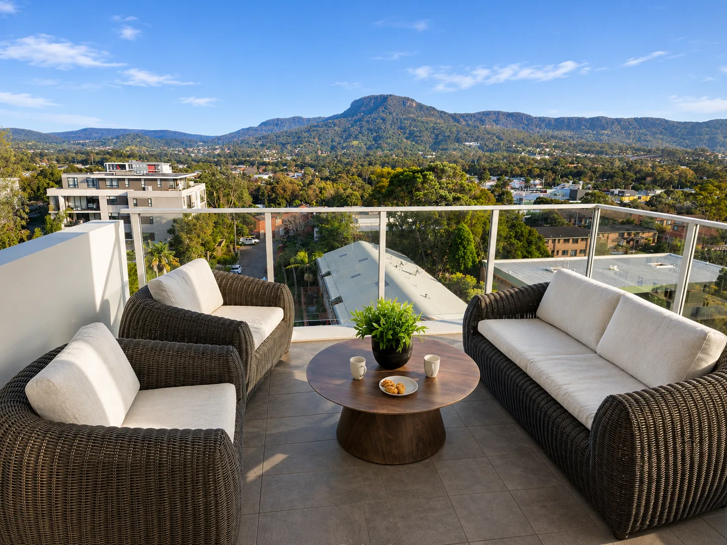 A balcony seating area overlooks a tree-filled landscape and distant mountain.