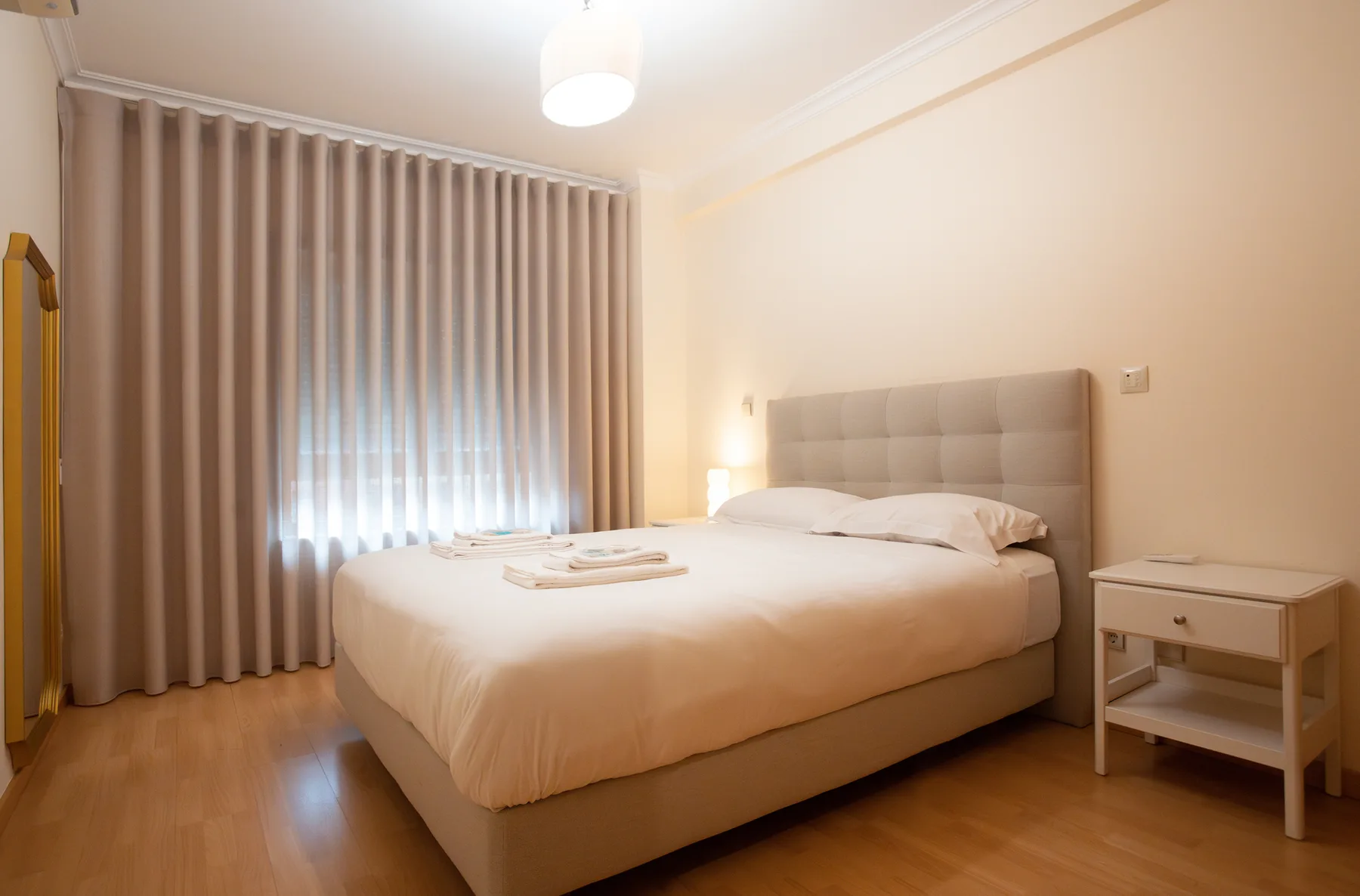 A bedroom with a large bed, bedside table, and floor-length curtains.