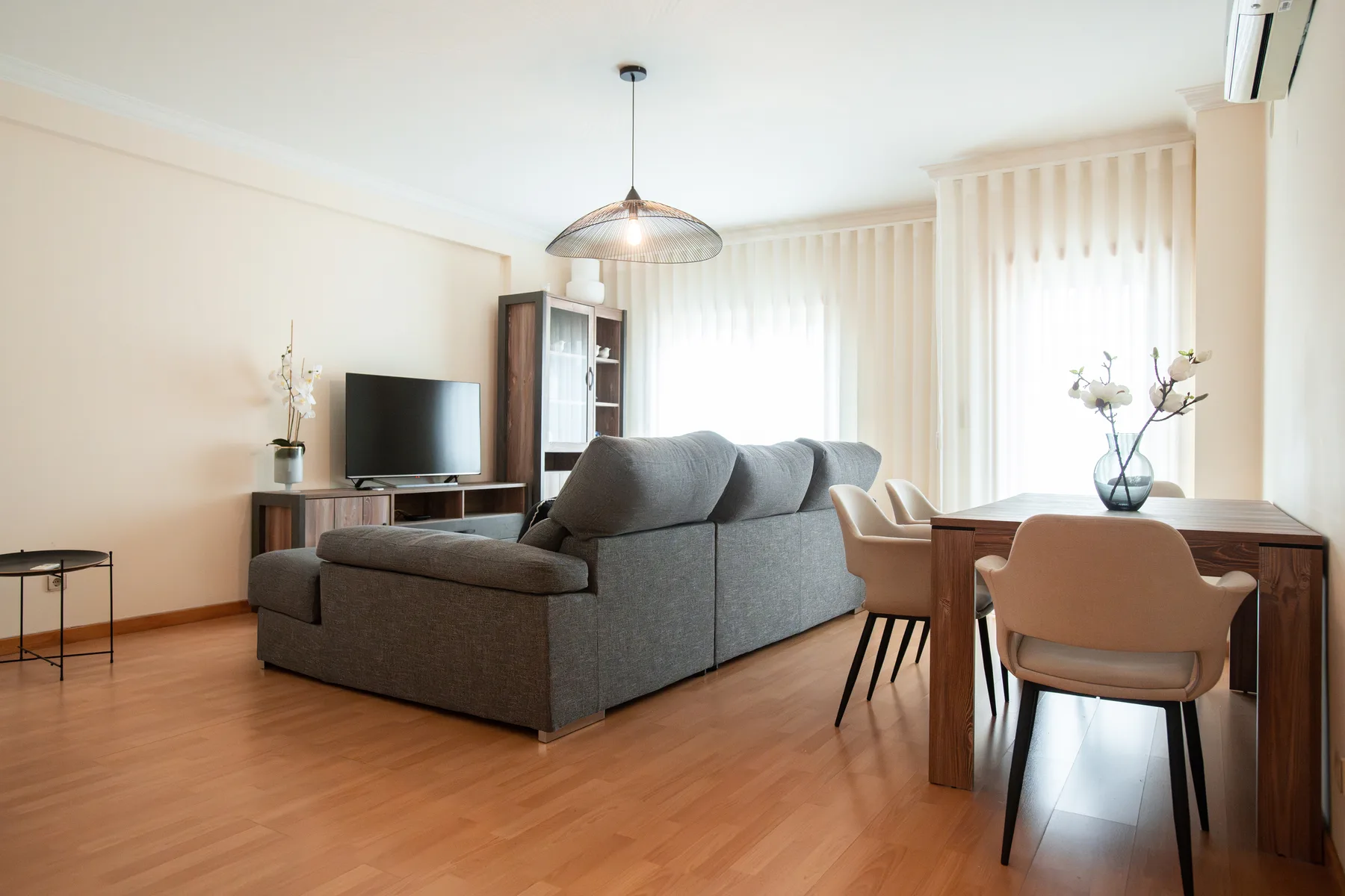 A living and dining area with gray seating, a television, and a wooden table.
