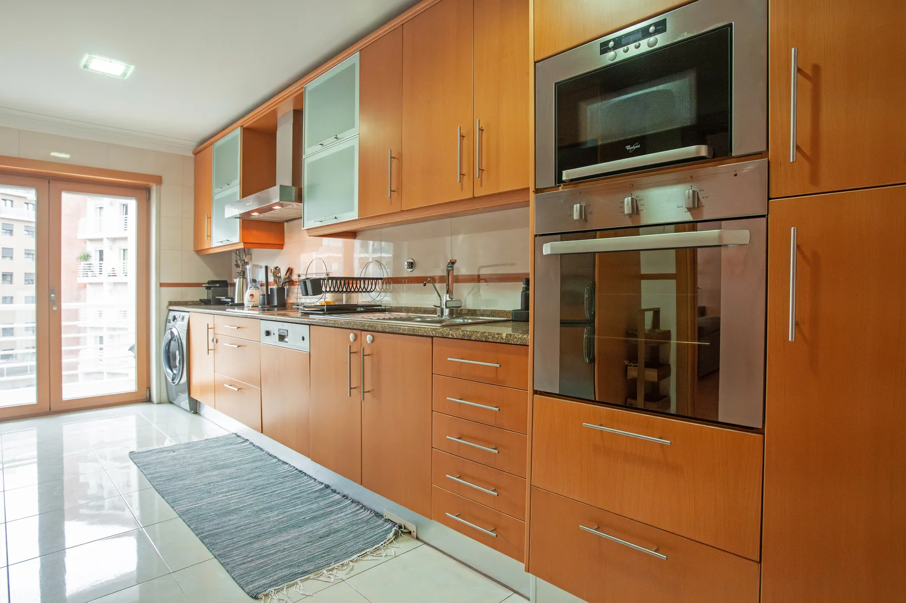 A kitchen with wooden cabinets, built-in appliances, and a long floor mat.