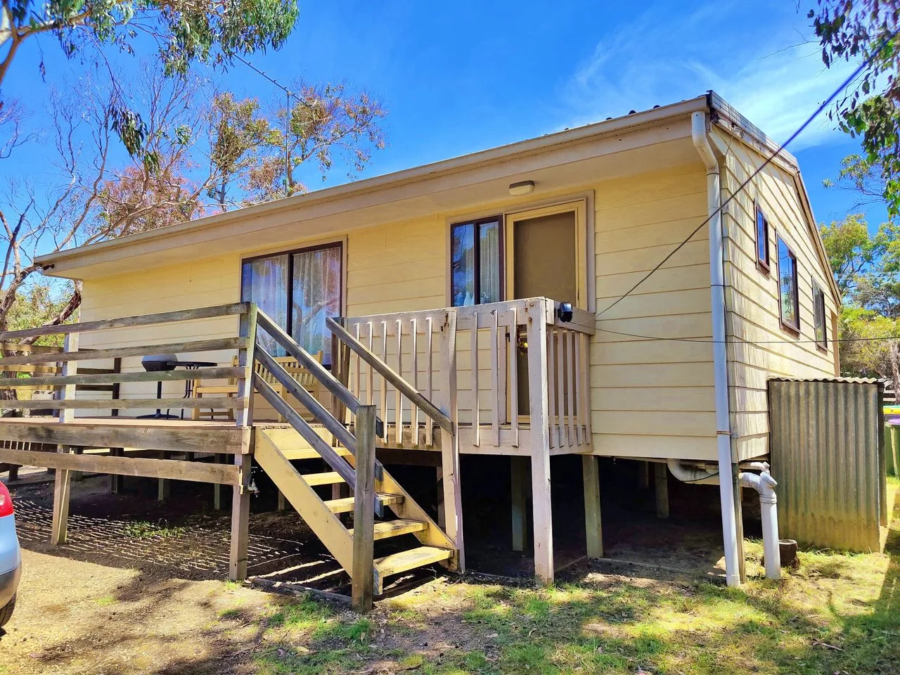 A raised cottage with a wooden deck and exterior stairs.