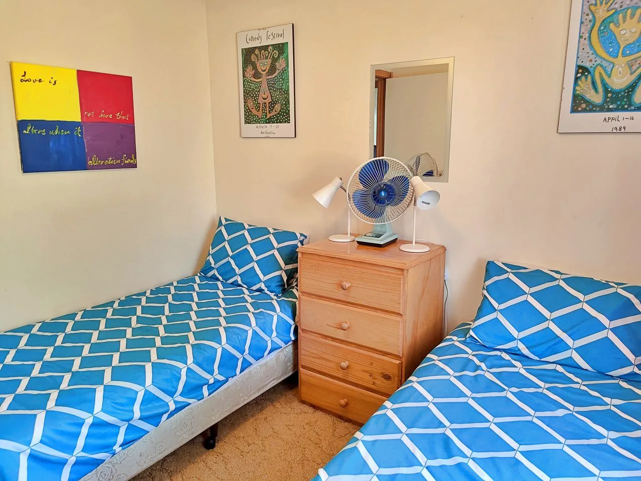 A twin bedroom with blue patterned bedding and a wooden bedside dresser.