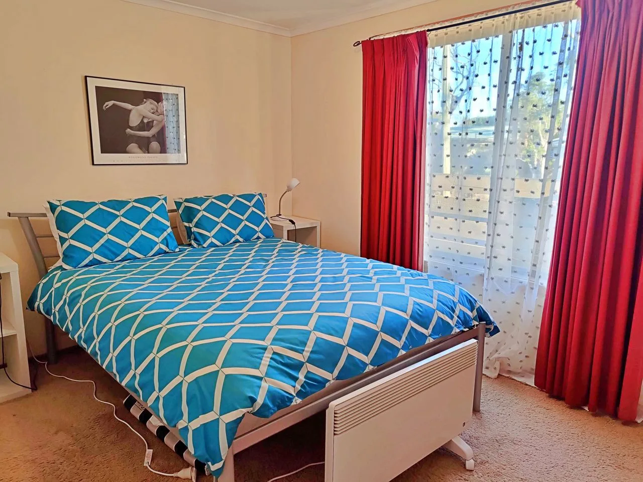 A bedroom with blue patterned bedding beside a window with red curtains.