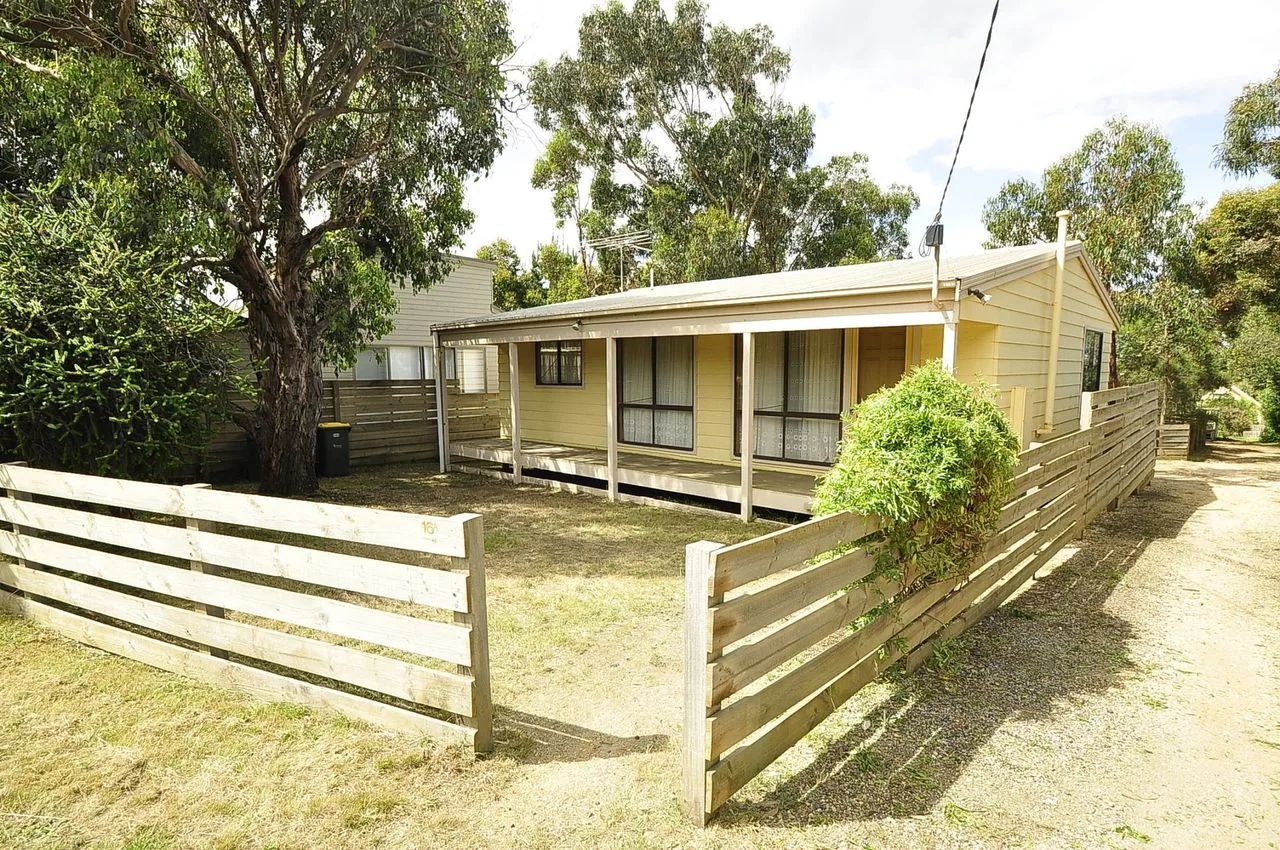 A pale single-story house sits behind a low wooden fence.