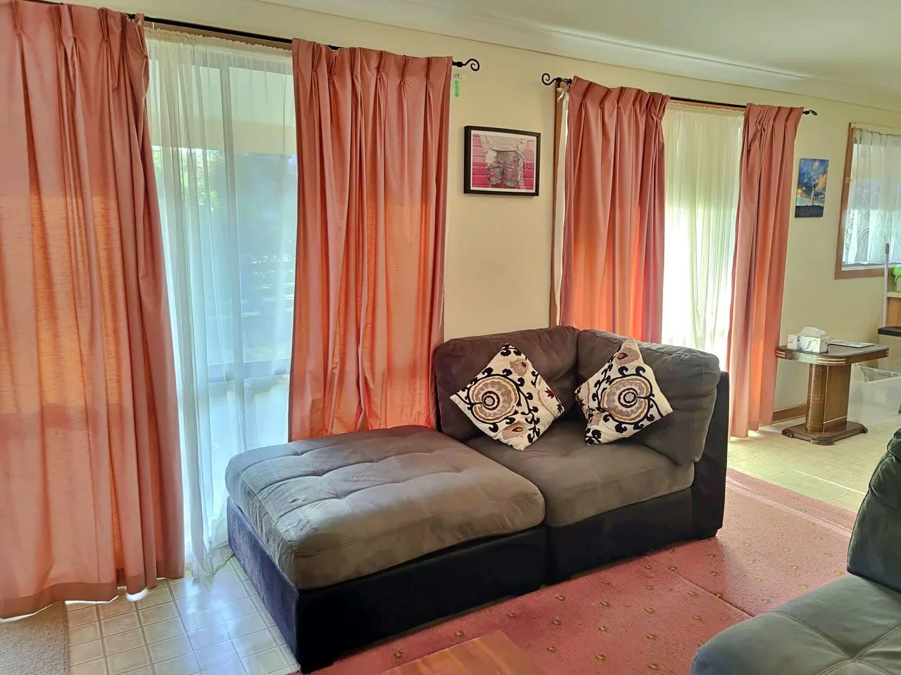 Living room with seating, coral curtains, and large windows.