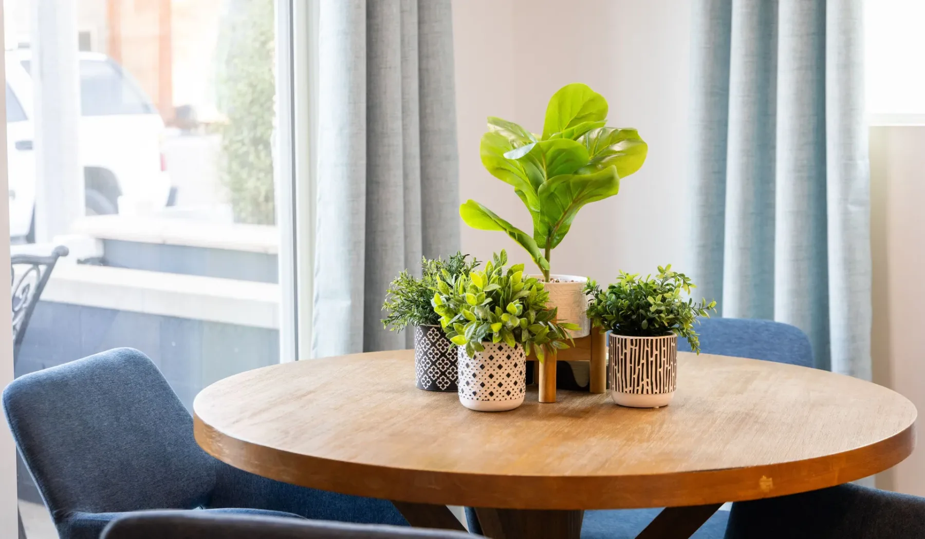 Una mesa redonda de madera con plantas en macetas está junto a una ventana.