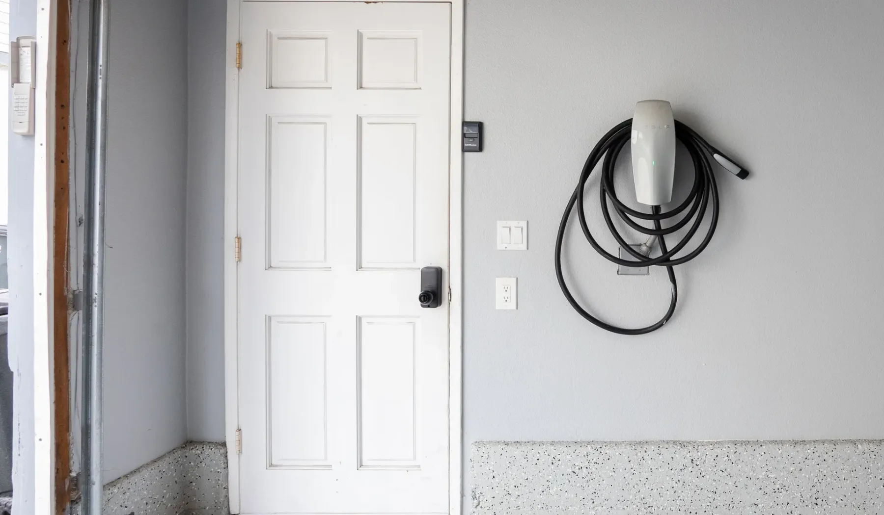 Una puerta blanca con paneles y un cable de carga montado en la pared de un garaje.