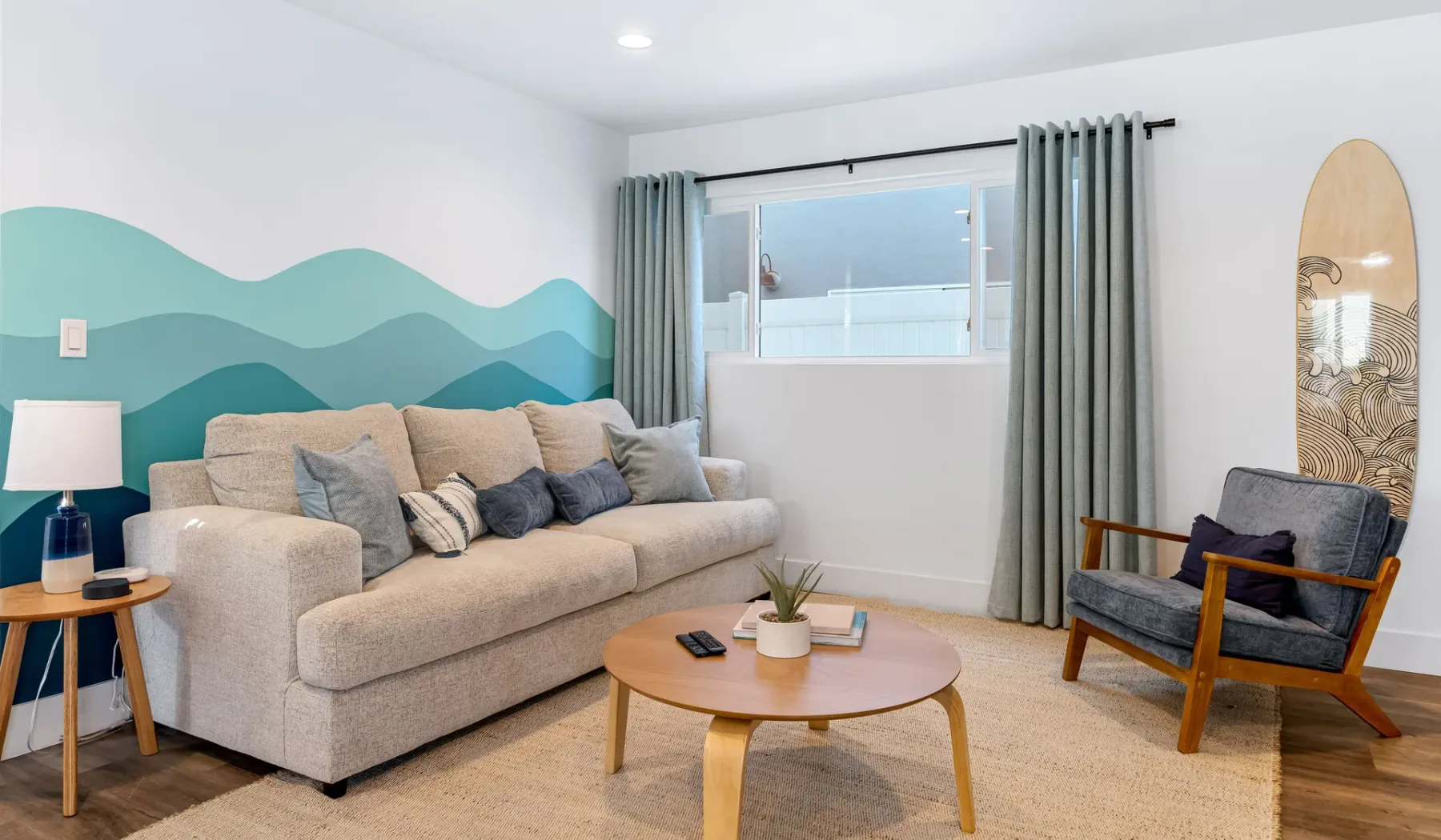 Una sala de estar con un sofá beige, un sillón y un mural de montañas.