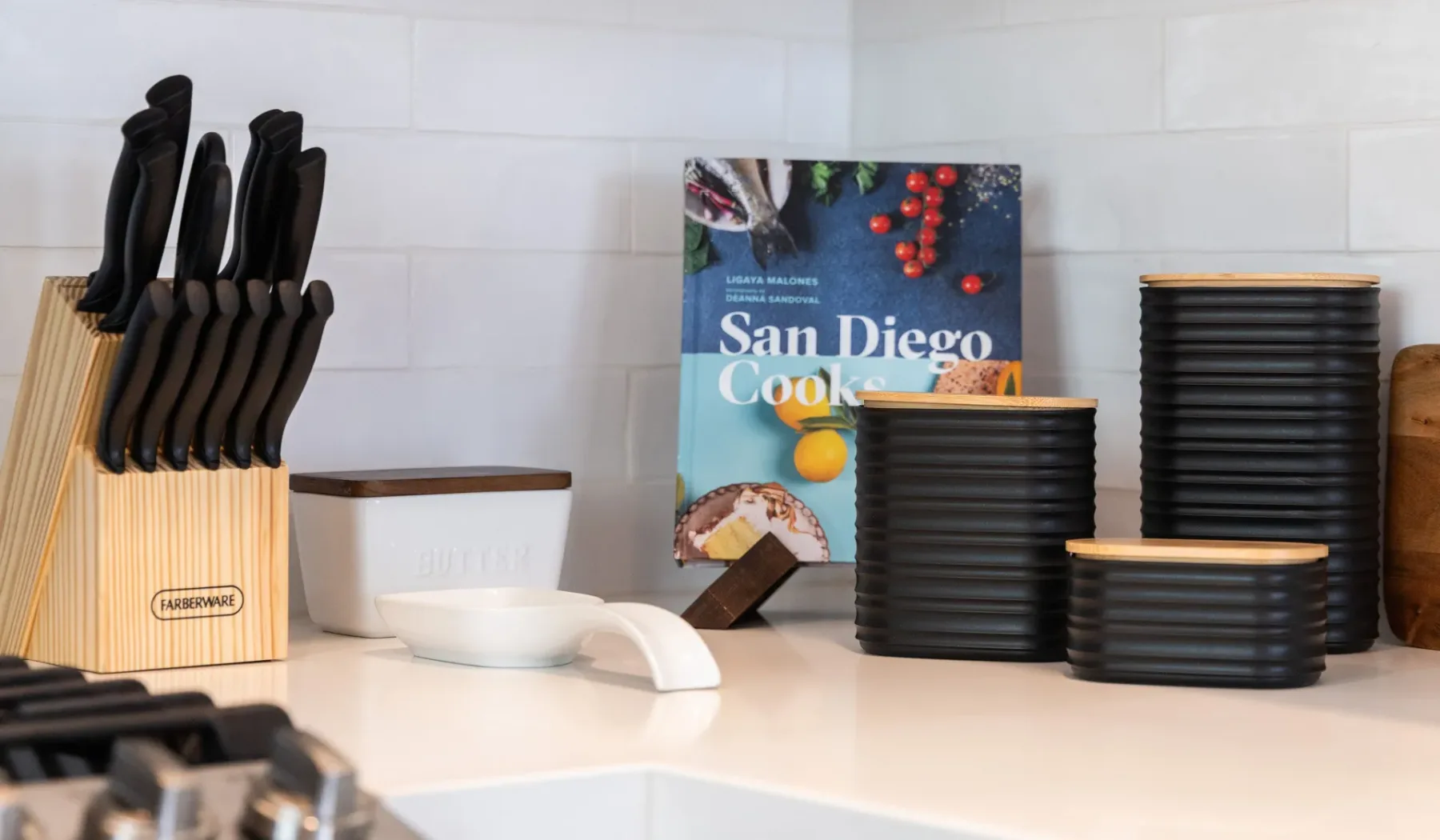 Una encimera de cocina muestra un bloque de cuchillos, platos apilados y un libro de cocina.